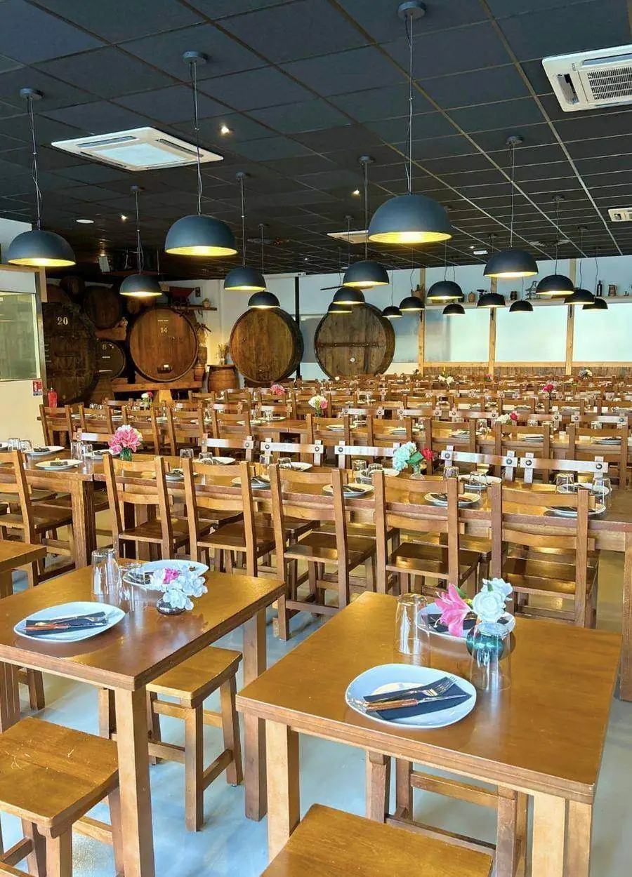 La grande salle du restaurant : longues tables de bois, suspensions noires, fûts en fond de salle