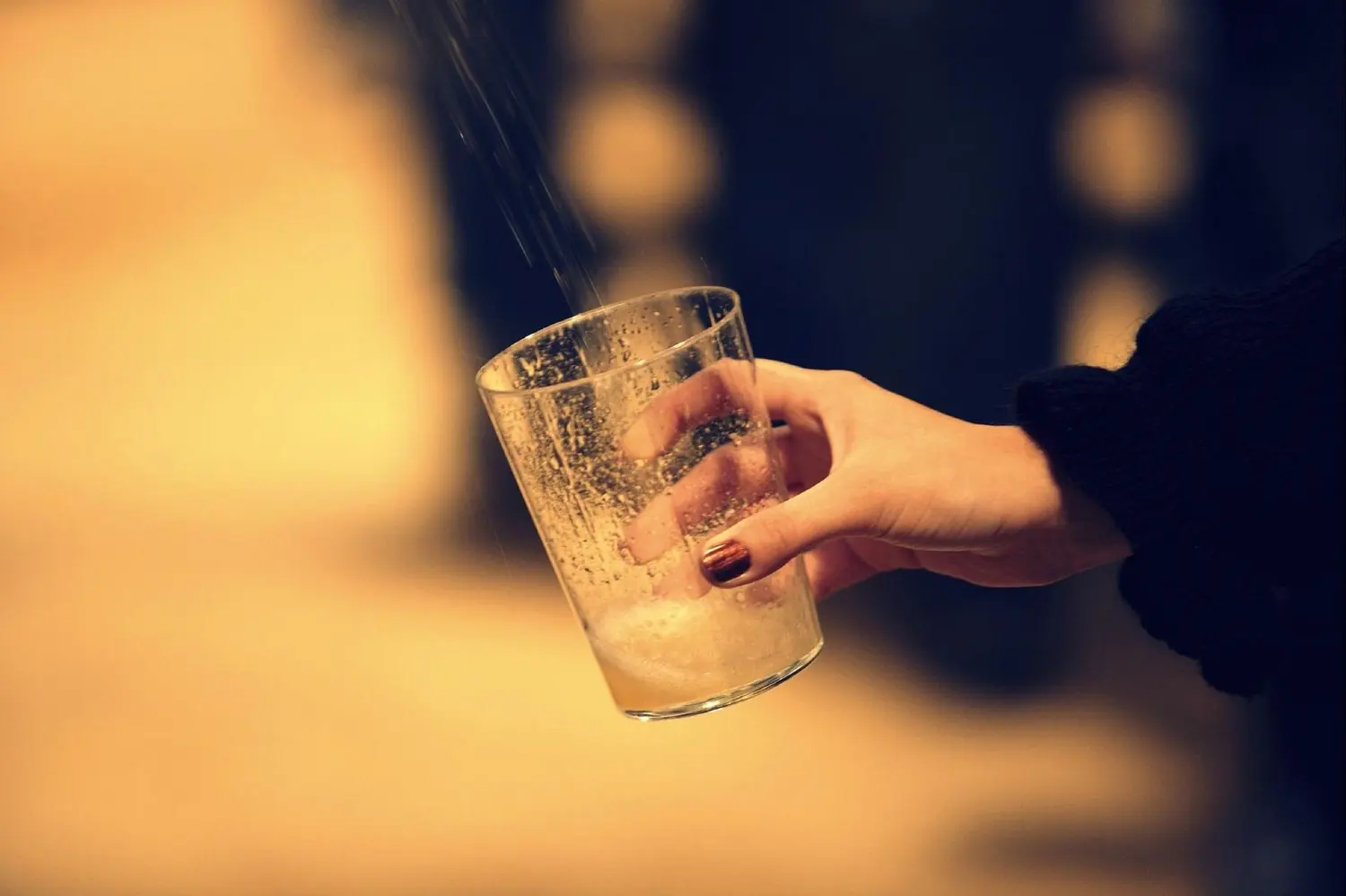 Une main tend un verre incliné sous le jet de cidre jaillissant du fût, dans la lumière dorée du chai